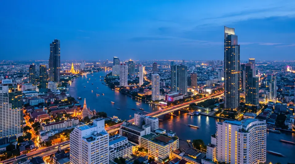 Bangkok skyline at blue hour seen from a rooftop, the Chao Phraya River curving through the city